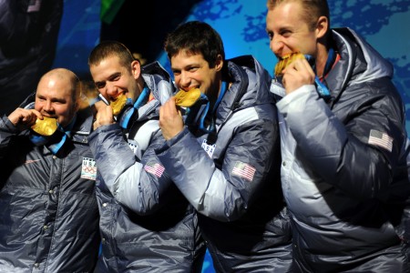 Former U.S. Army World Class Athlete Program bobsledder Steven Holcomb and teammates Justin Olsen, Steve Mesler and Curt Tomasevicz bite their gold medals Saturday night at Whistler Medals Plaza after winning the Olympic four-man bobsled crown earlier in the day at Whistler Sliding Centre at the 2010 Winter Olympics.