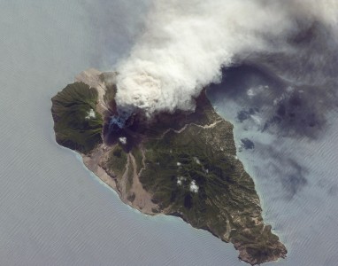 This oblique astronaut photograph from the International Space Station (ISS) captures a white-to-grey ash and steam plume extending westwards from the volcano. Oblique images are taken by astronauts looking out from the ISS at an angle, rather than looking straight downward toward the Earth (a perspective called a nadir view), as is common with most remotely sensed data from satellites. An oblique view gives the scene a more three-dimension quality, and provides a look at the vertical structure of the volcanic plume. While much of the island is covered in green vegetation, grey deposits that include pyroclastic flows and volcanic mud-flows (lahars) are visible extending from the volcano toward the coastline. When compared to its extent in earlier views, the volcanic debris has filled in more of the eastern coastline. Urban areas are visible in the northern and western portions of the island; they are recognizable by linear street patterns and the presence of bright building rooftops. The silver-grey appearance of the Caribbean Sea surface is due to sun-glint, which is the mirror-like reflection of sunlight off the water surface back towards the hand-held camera on-board the ISS. The sun-glint highlights surface wave patterns around the island.
