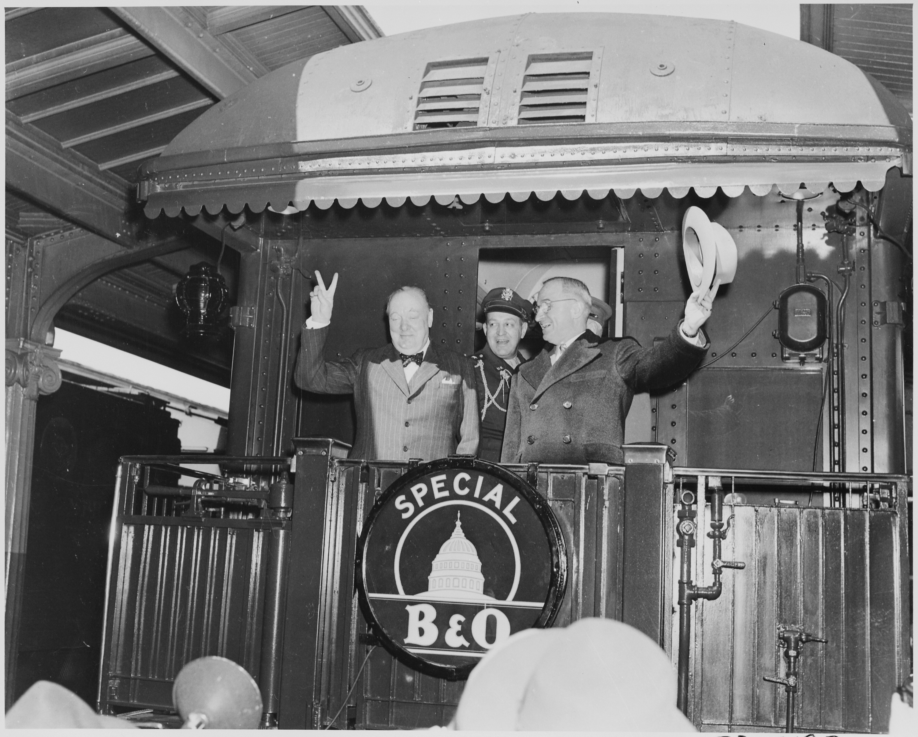 Photograph of President Truman waving his hat and Winston Churchill flashing his famous 