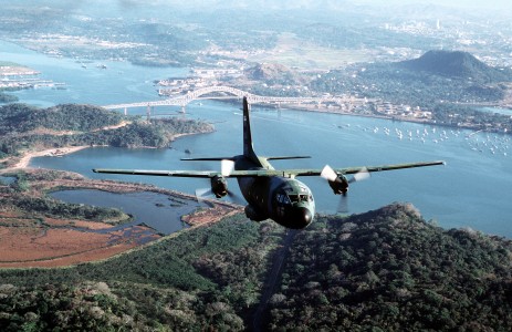 A downward front view of a C-27A Spartan in flight over water and tree tops. Location: HOWARD AIR FORCE BASE