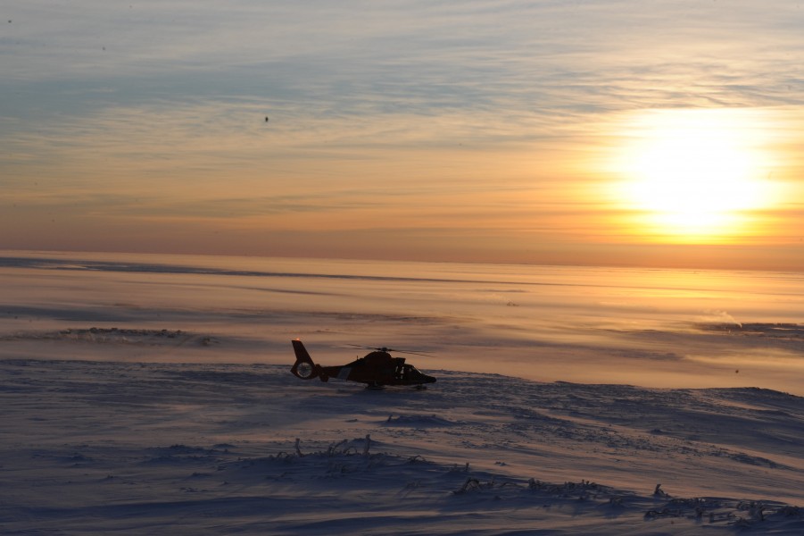 A U.S. Coast Guard MH-60 Dolphin helicopter crew ascends from a mountain with the city of Nome, Alaska, in the background Jan 120116-G-YE680-341