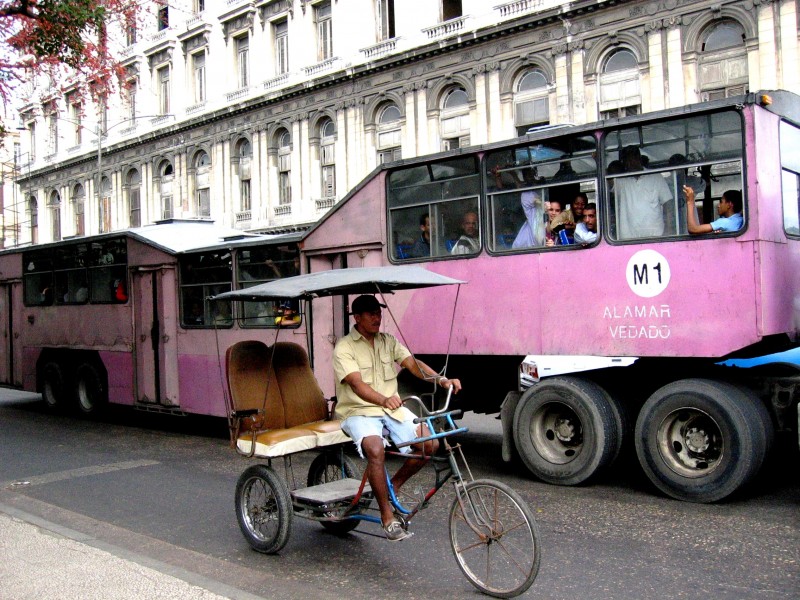 A bike taxi and large bus street scene in Cuba