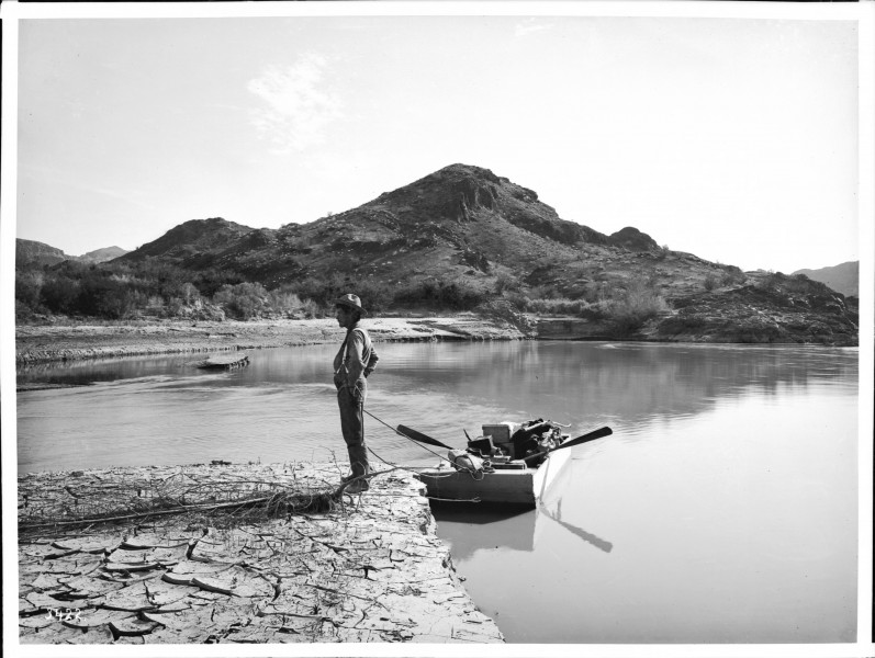 Man standing on shore next to a small ferry boat moored along the Colorado River in one of the Mojave canyons, California, 1900-1950 (CHS-3422)