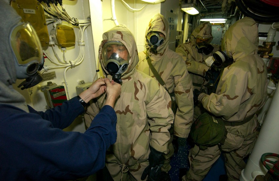 US Navy 030920-N-5471P-004 Damage Controlman 3rd Class Michael Muskett helps Ship's Serviceman 3rd Class Daniel Olaya don chemical protective gear