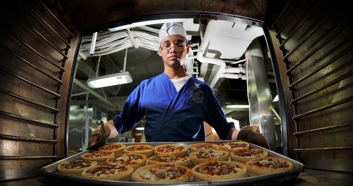 US Navy 080809-N-7981E-082 Culinary Specialist 3rd Class Gabriel Common, from Basile, La., takes pizzas out of the oven in the aft galley aboard the Nimitz-class aircraft carrier USS Abraham Lincoln (CVN 72)