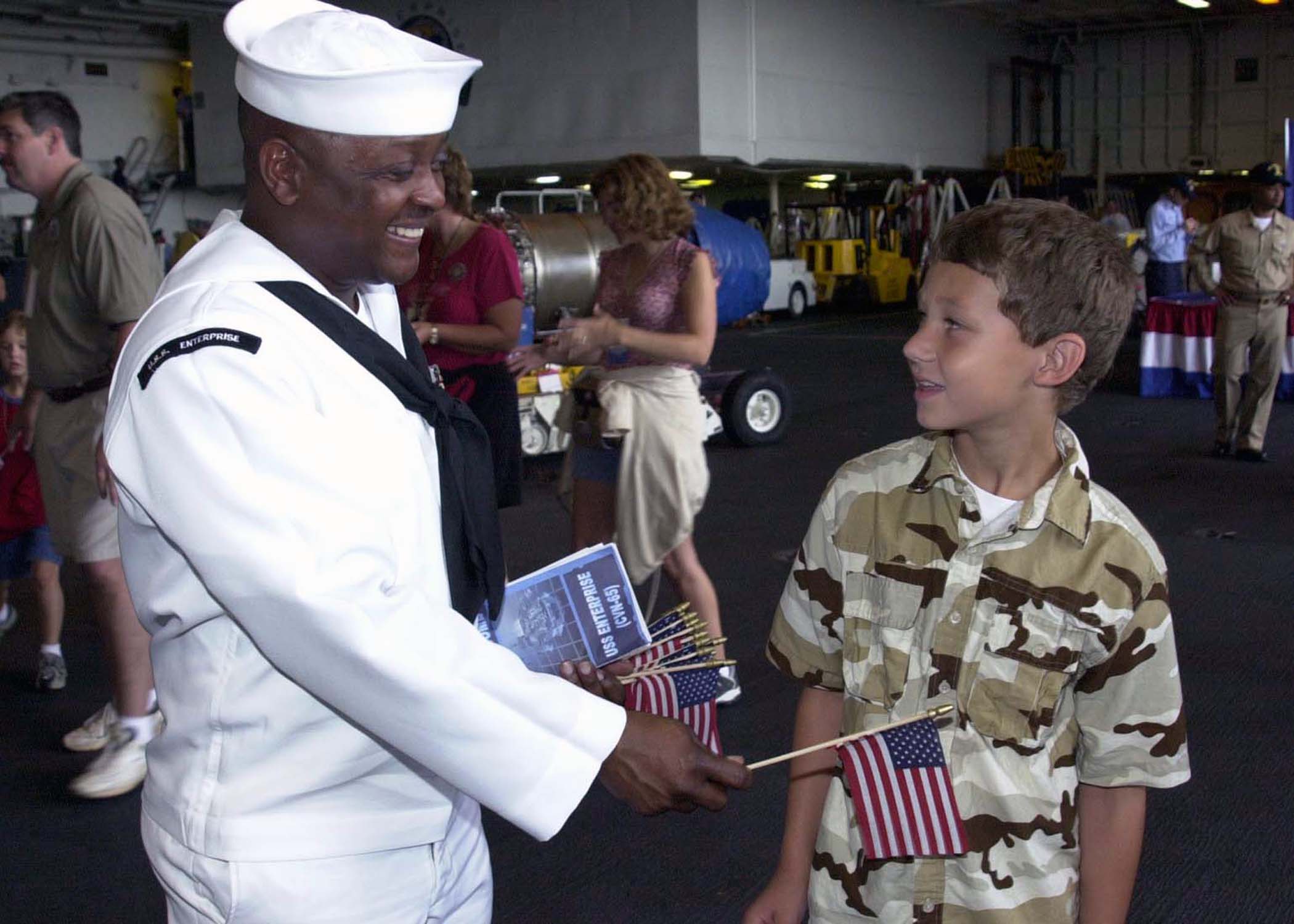 US Navy 040429-N-6268K-004 A Sailor gives a boy an American flag in the hangar bay aboard the aircraft carrier USS Enterprise (CVN 65)