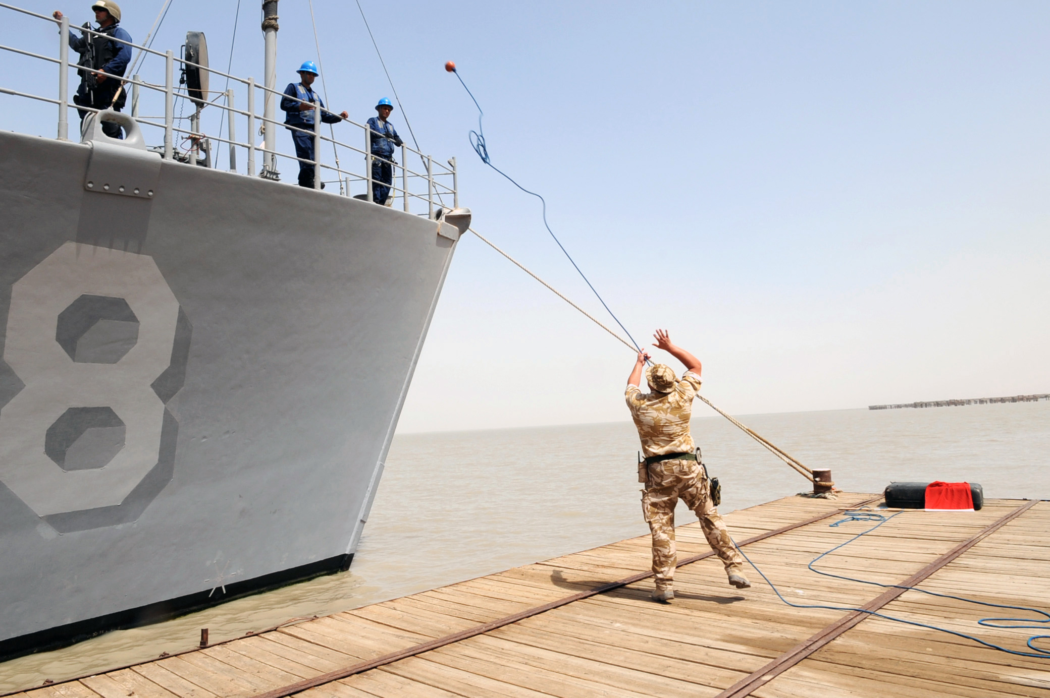 US Navy 090630-N-6814F-057 British Royal Navy Leading Seaman Lee Noak throws a messenger line to the deck of mine countermeasure ship USS Scout (MCM 8) as it pulls into Umm Qasr, Iraq