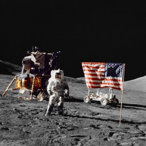 Astronaut Harrison H. Schmitt, lunar module pilot, stands near the deployed United States flag on the lunar surface during Extravehicular Activity (EVA) of NASA's final lunar landing mission in the Apollo series. The Lunar Module (LM) is at left background and the Lunar Roving Vehicle (LRV) at right background (partially obscured). The photo was made by astronaut Eugene A. Cernan, commander.