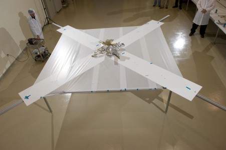 NanoSail-D deployment, part 2: The sail, made of extremely lightweight gossamer fabric manufactured by ManTech SRS of Huntsville, AL, begins to unfurl supported by rigid trac booms provided by the Air Force Research Laboratory. The sail material is much thinner than a piece of paper (less than 1/16th the thickness of a human hair) and coated with an extremely thin layer of aluminum to enhance its ability to reflect solar energy. Here on Earth, gravity prevents the doors from fully opening but in the microgravity of space, the doors will swing open freely. For this test, engineers used rubber bands to secure the doors in the open position.