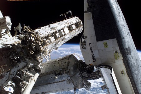 This image features a view of Space Shuttle Discovery docked to the Pressurized Mating Adapter 2 (PMA-2) on the Destiny laboratory of the international space station. The Crew Equipment Translation Aid (CETA) cart and the Mobile Base System (MBS), mounted on the S0 truss, are visible at left. Part of the P1 truss is also visible in the background. Dwarfed by the station and shuttle, Japan Aerospace Exploration Agency (JAXA) astronaut Soichi Noguchi, STS-114 mission specialist, is visible near the PMA-2 during the missionвЂ™s third session of extravehicular activity (EVA). The blackness of space and a blue and white Earth form the backdrop for the image.