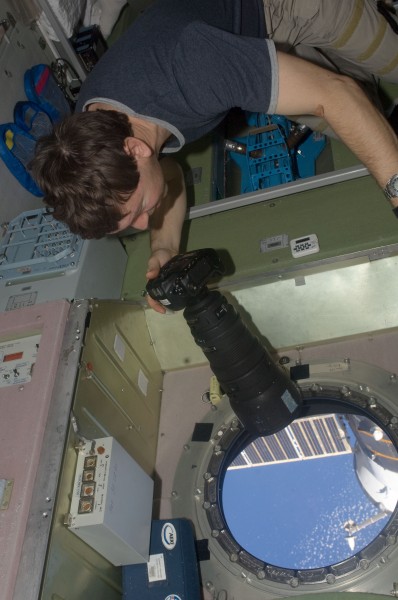ISS-19 Michael Barratt uses a still camera at a window in the Zvezda Service Module