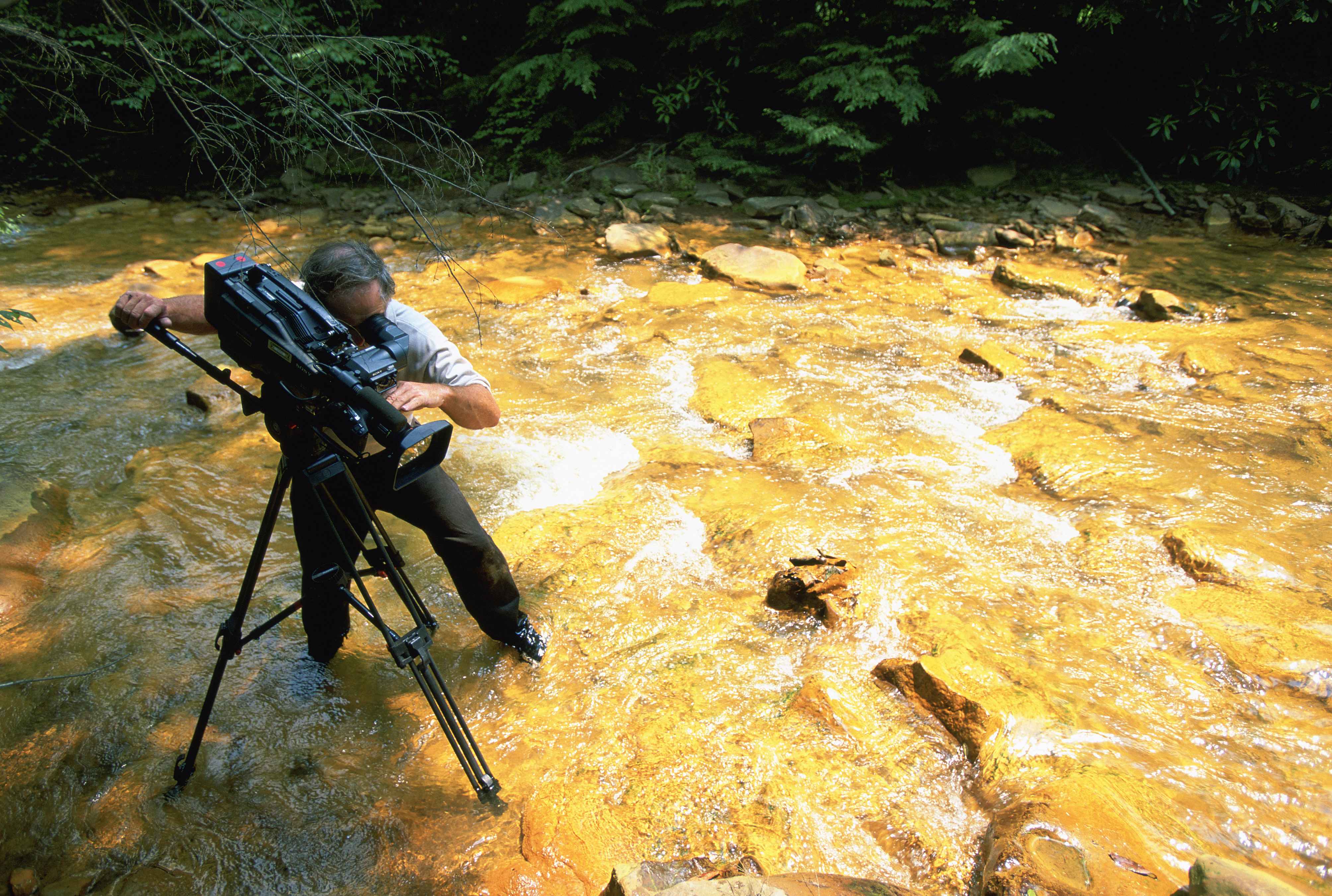 Videographer recording effects of acid mine runoff in stream