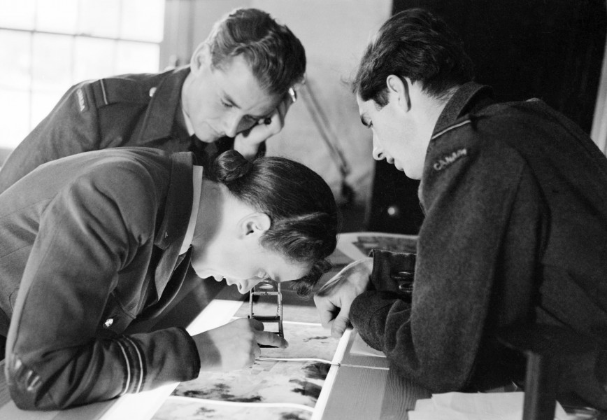 A WAAF flight officer photographic interpreter with two Canadian pilots of a photographic reconnaissance squadron, examining newly-developed 8