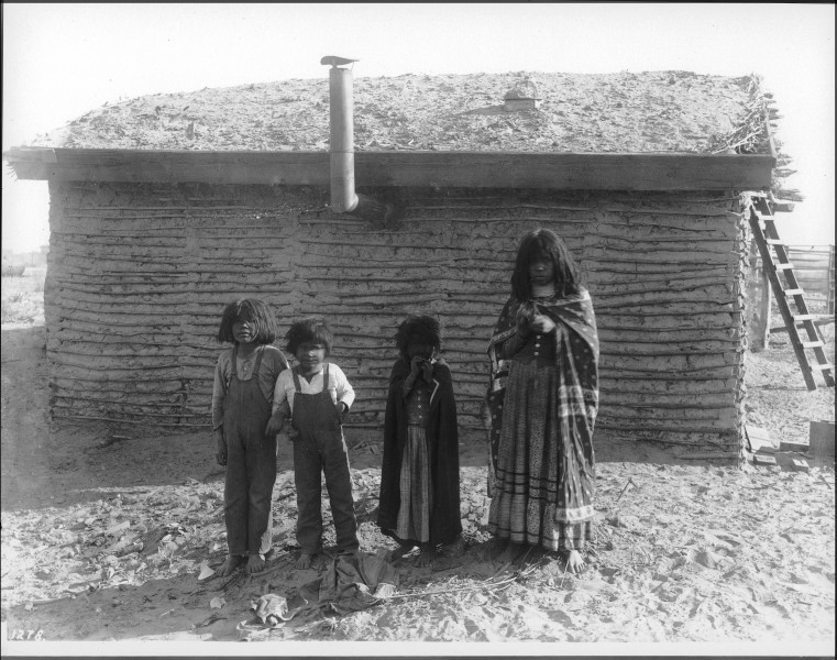 Four Mojave Indian children standing in front of a small dwelling with a thatched roof, near Yuma, ca.1900 (CHS-1278)