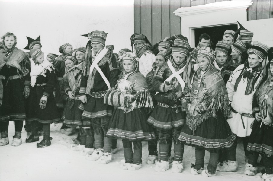 Group of sami in traditional costumes in front of a house