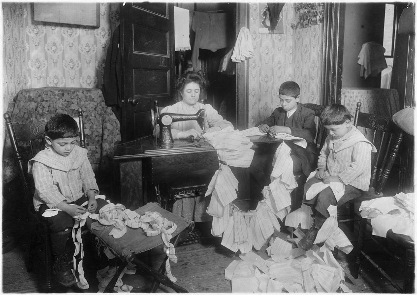 Making dresses for Campbell kids dolls in a dirty tenement. The older boy, about 12 years old, operates the machine... - NARA - 523529