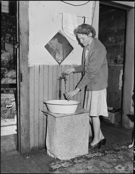Young wife of a miner drawing water at the tap in her kitchen. This tap was installed by a former tenant, few houses... - NARA - 540942