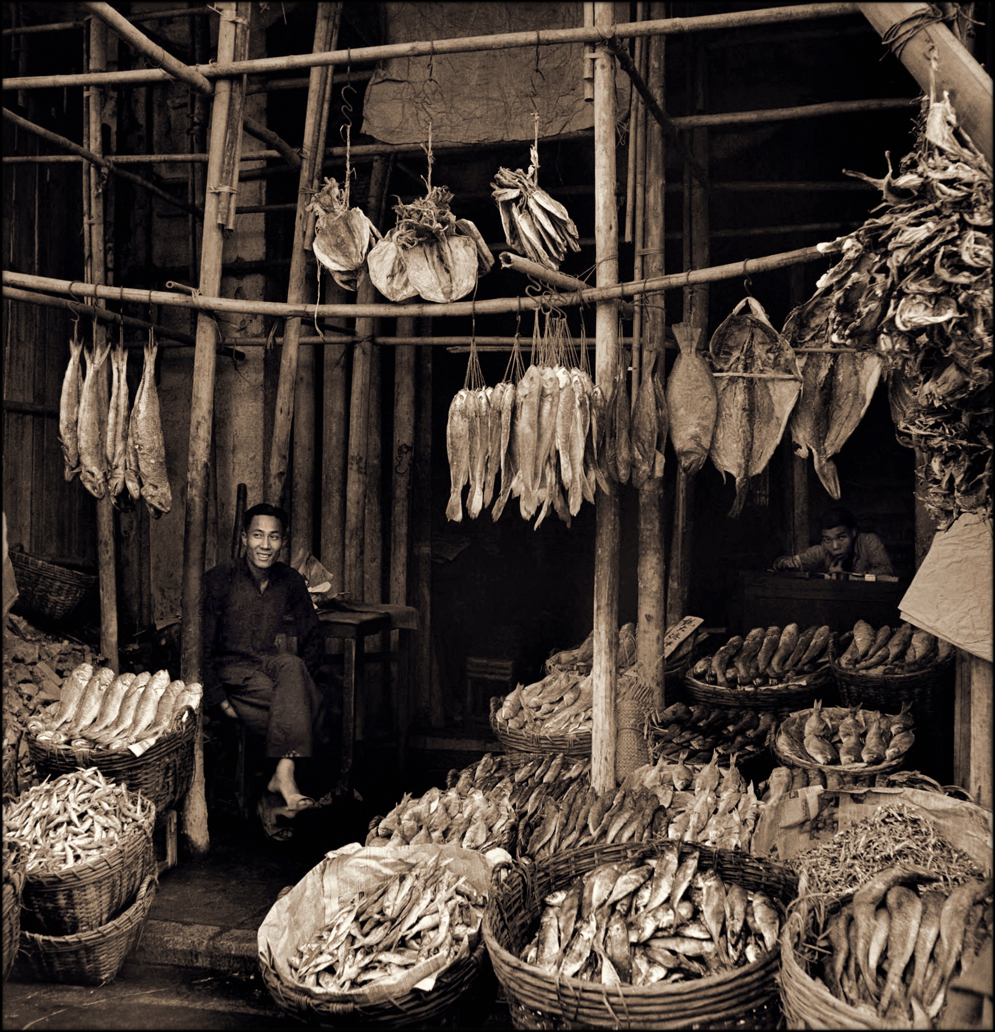 Seated Man Amid Baskets Of Fish & Hanging Dried Fish, Eastern Districts, Hong Kong Island (c1946) Hedda Morrison (RESTORED) (4169611255)