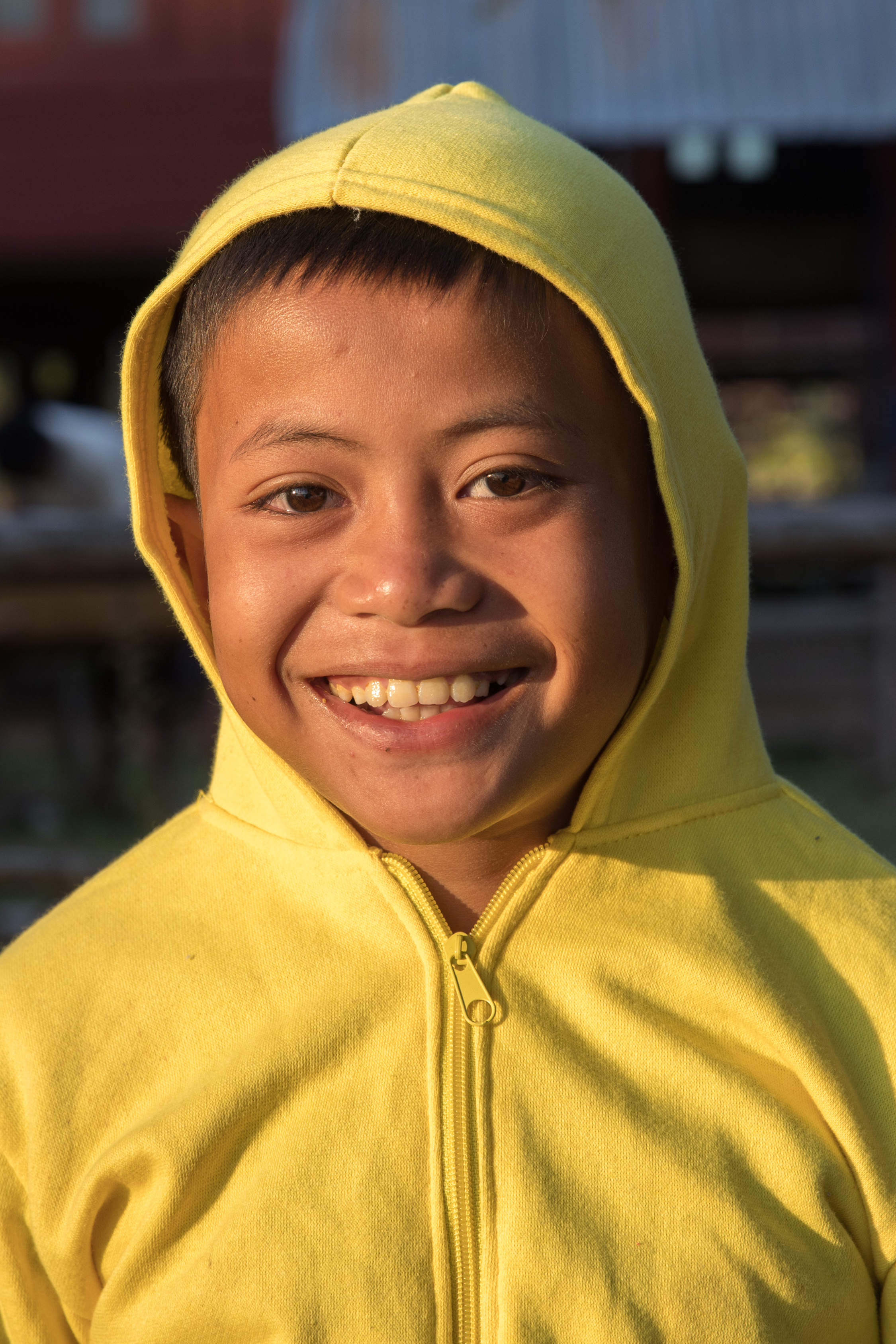 Portrait in sunshine at golden hour of a smiling boy wearing a yellow sweater with hood pulled up in Laos