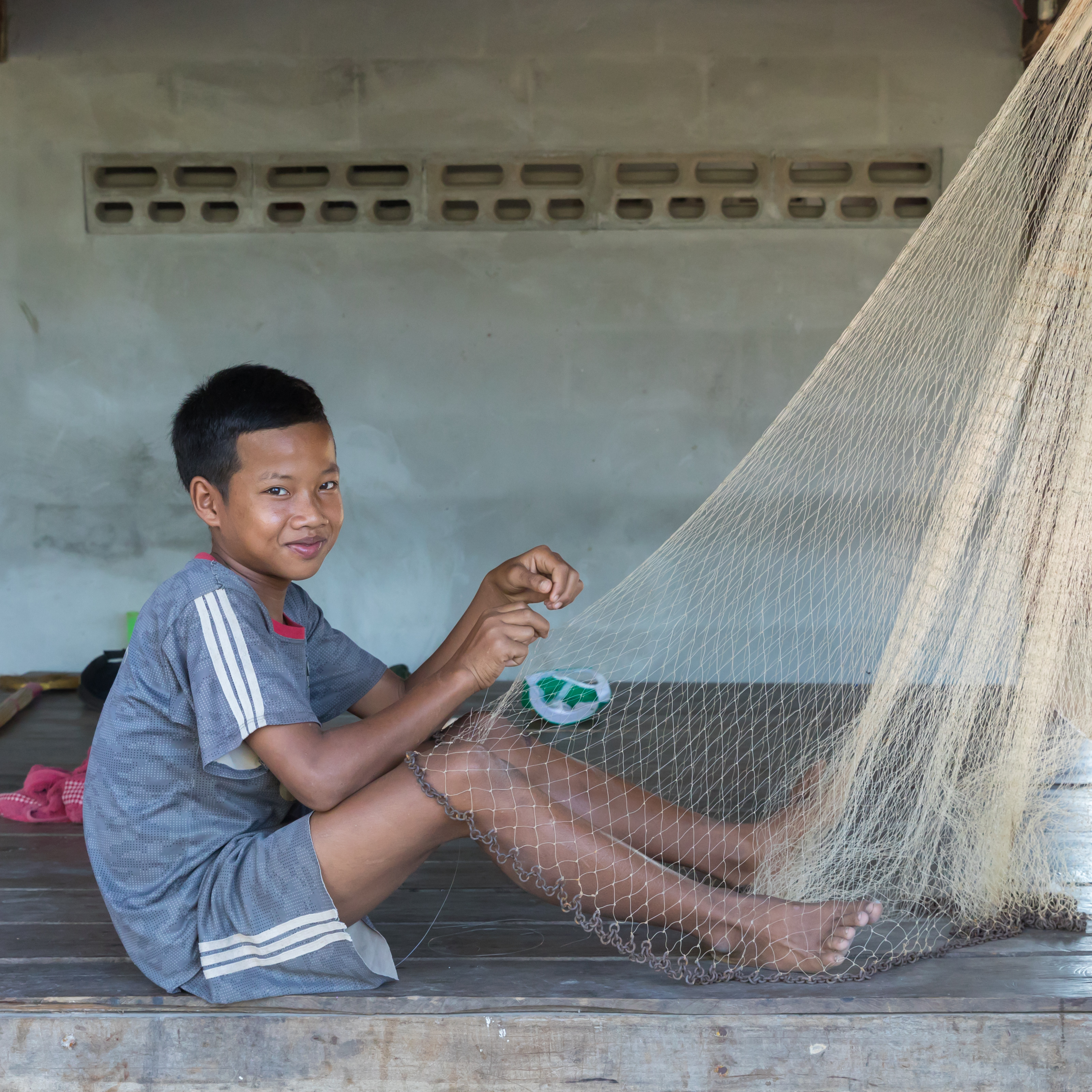 Sitting boy weaving a fishing net in Laos