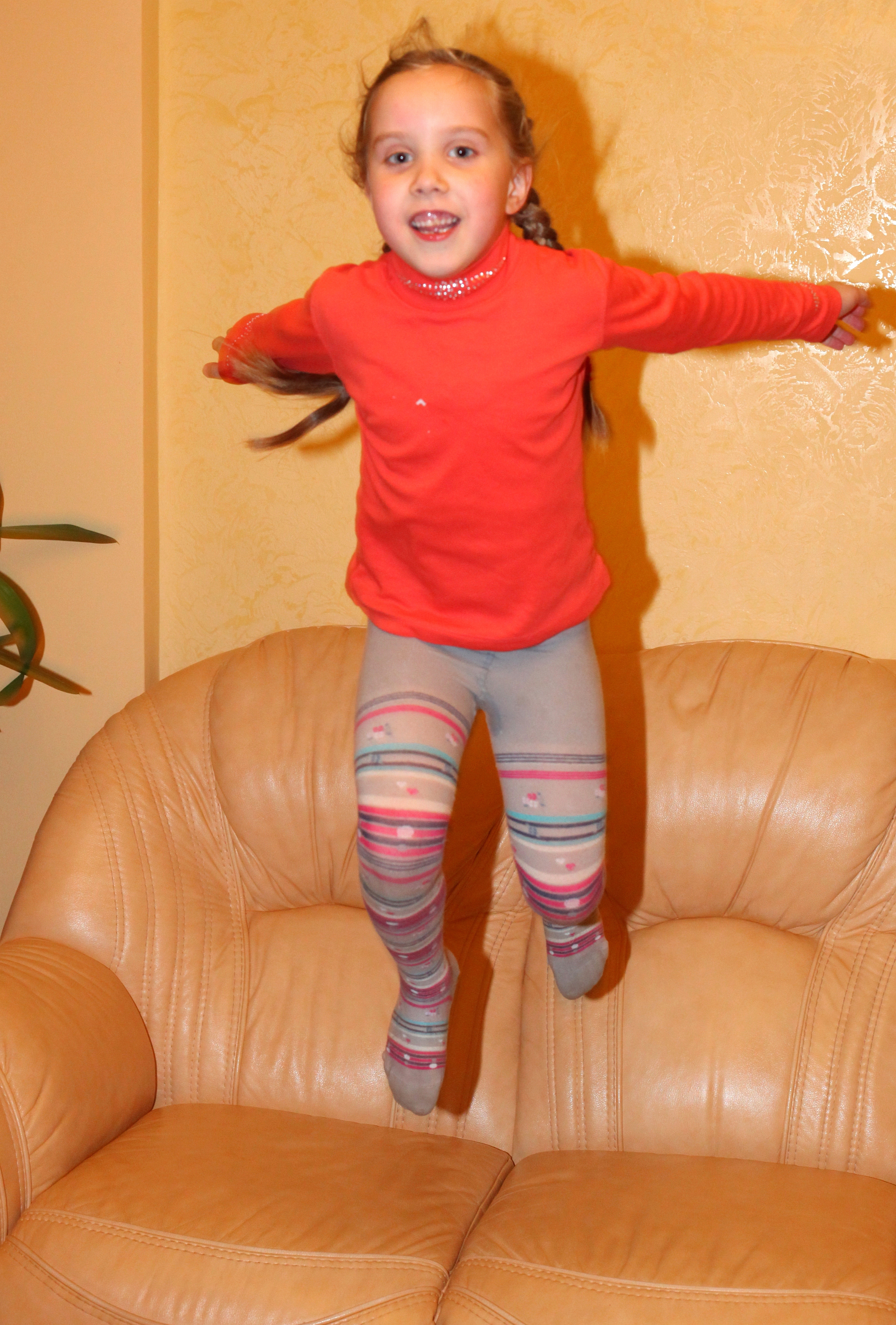 a young cute blond child girl jumping from the sofa