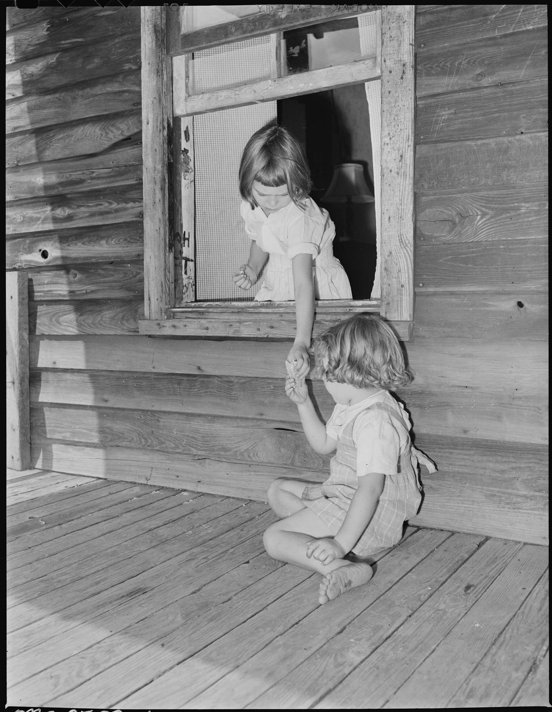 Wanda Lee Sergent hands her sister, Bobbie Jean, an ice cream cone through the window opening from the front porch to... - NARA - 541318