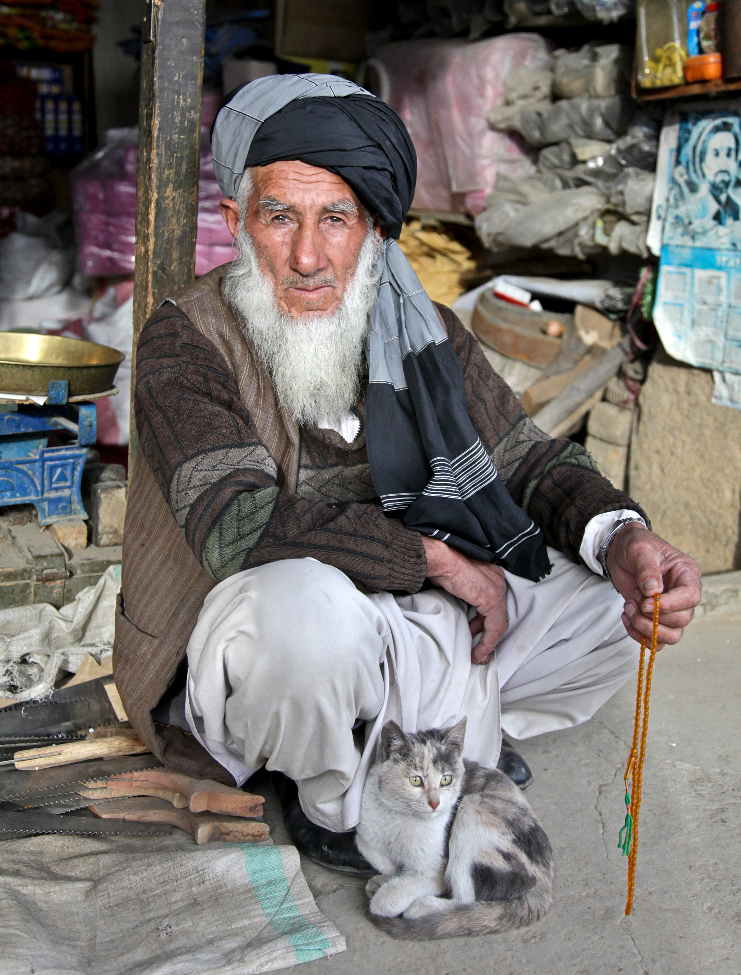 An Afghan elder and his cat sit outside his store at the Anaba bazaar in Panjshir province, Afghanistan