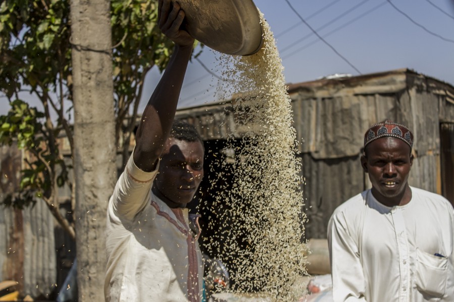 A man removes chaff from rice while his friend watches