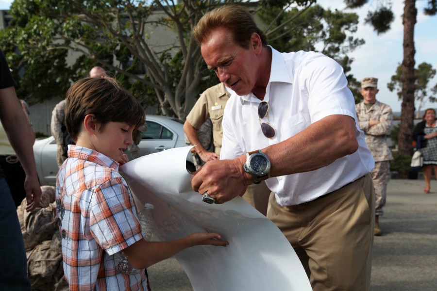 Arnold Schwarzenegger signs a young boy’s “The Expendables 2” poster, 2012