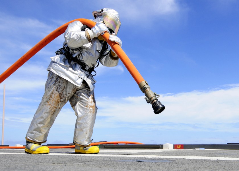 Defense.gov News Photo 110927-N-WJ771-108 - U.S. Navy Petty Officer 2nd Class Joshua B. Cary carries a charged fire hose across the flight deck of the amphibious transport dock ship USS Denver