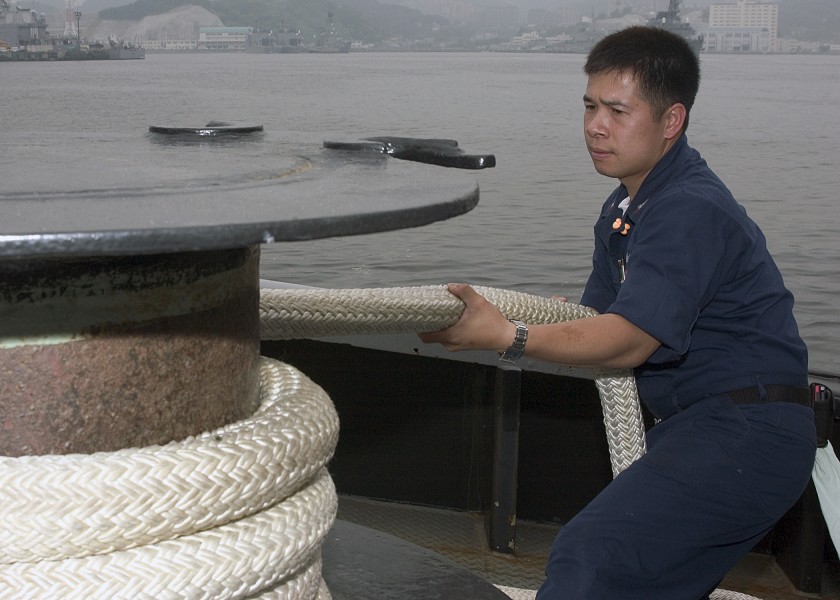 US Navy 060621-N-5686B-003 Electrician's Mate 2nd Class Zhixian Zhong wraps the mooring line around the capstan during an evolution aboard the tugboat USS Opelika (YTB 798)