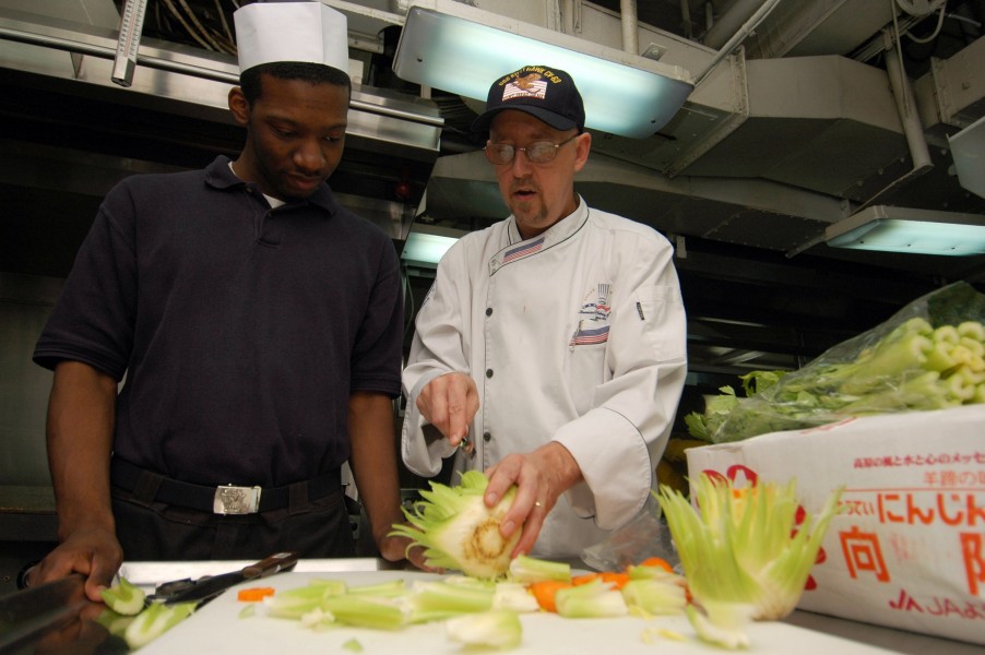US Navy 071022-N-5387K-007 Chef Ray Duey instructs Culinary Specialist Seaman Keyon Burrell on how to make a vegetable garnish aboard USS Kitty Hawk (CV 63)