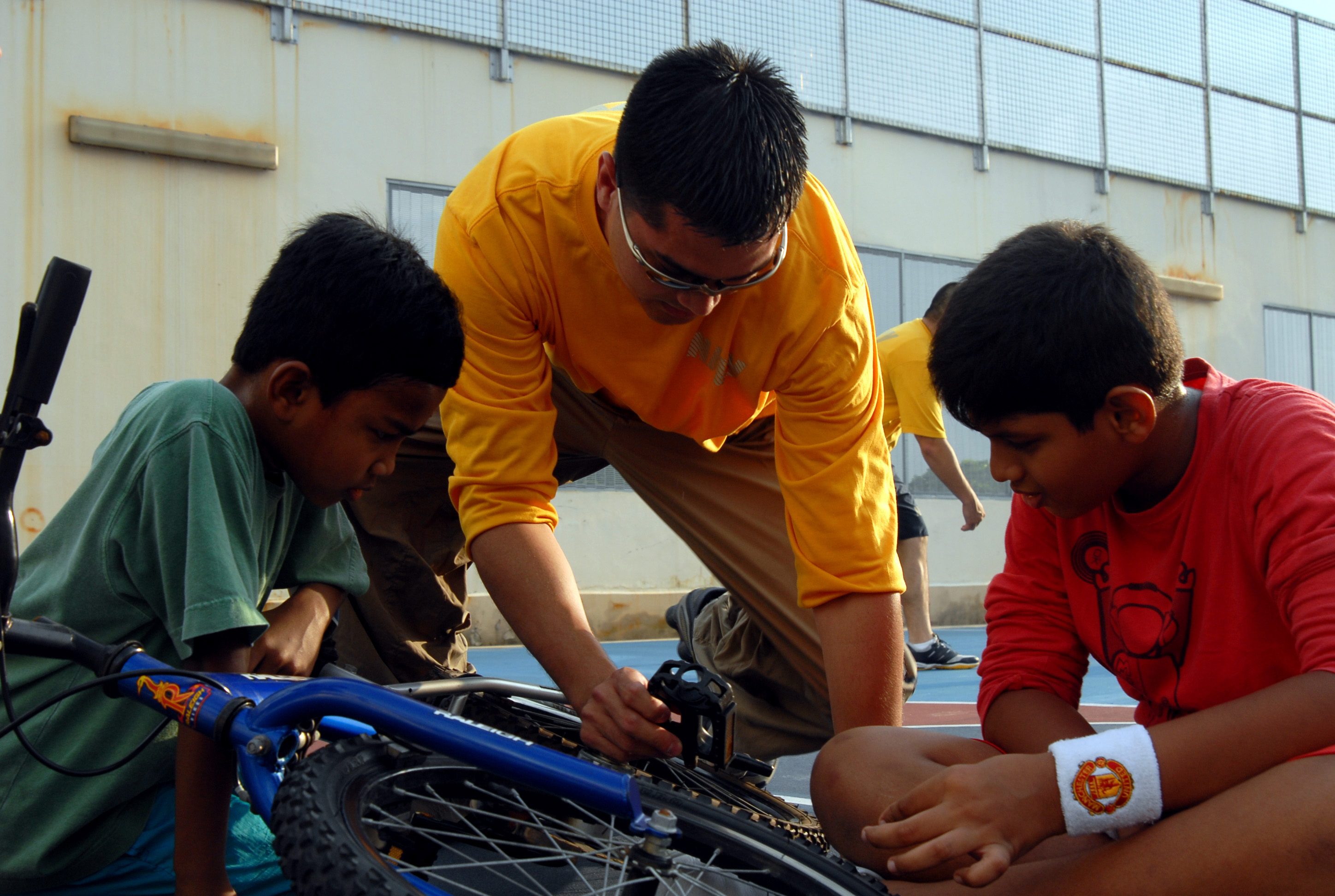 US Navy 091031-N-4908A-245 Electronics Technician 2nd Class Ryan James, assigned to the amphibious command ship USS Blue Ridge (LCC 19), helps a child fix his bicycle
