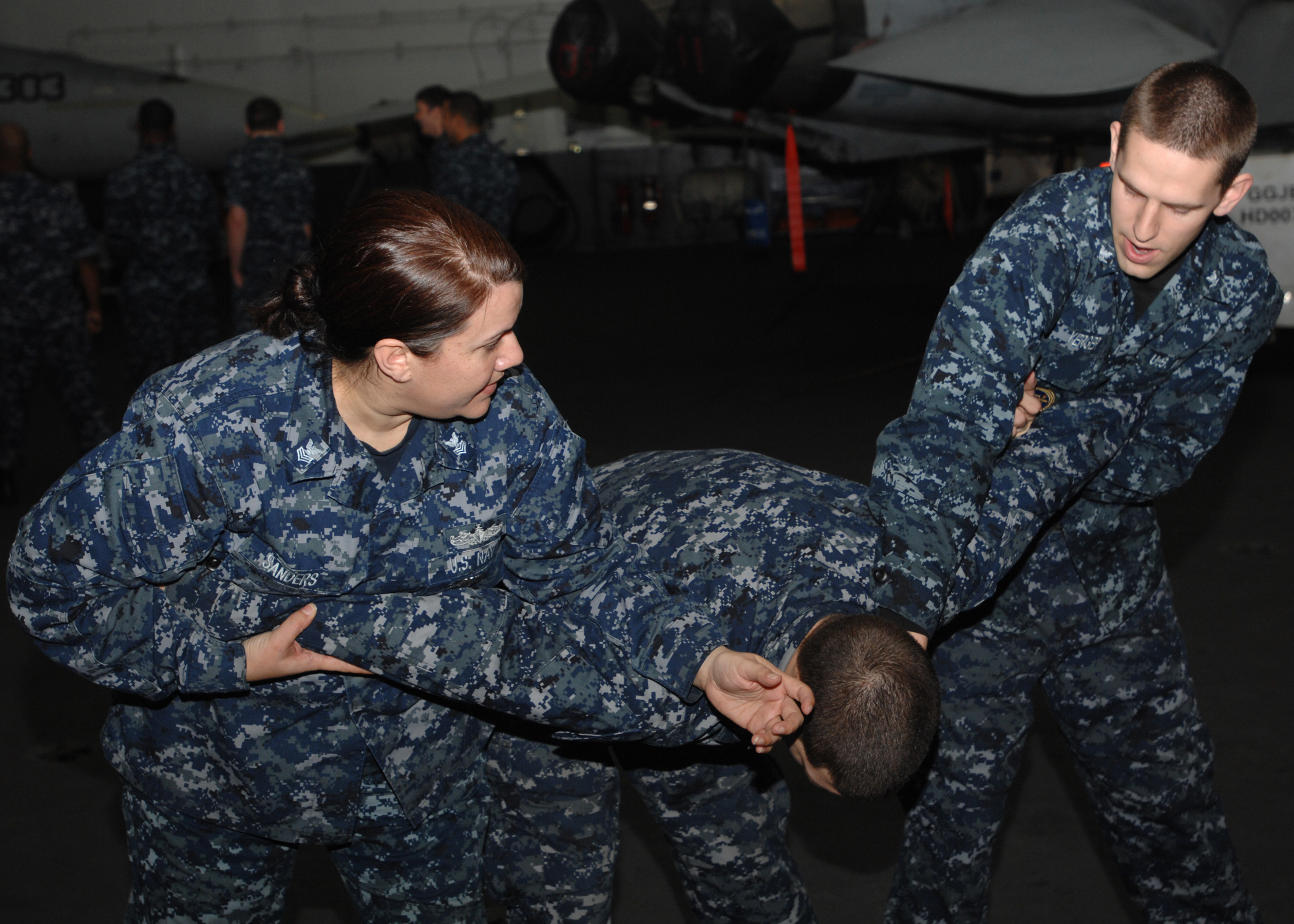 US Navy 100125-N-2798F-002 Master-at-Arms 1st Class Andria Sanders and Aviation Ordnanceman 3rd Class Patrick Yeger practice self-defense techniques on a fellow Sailor
