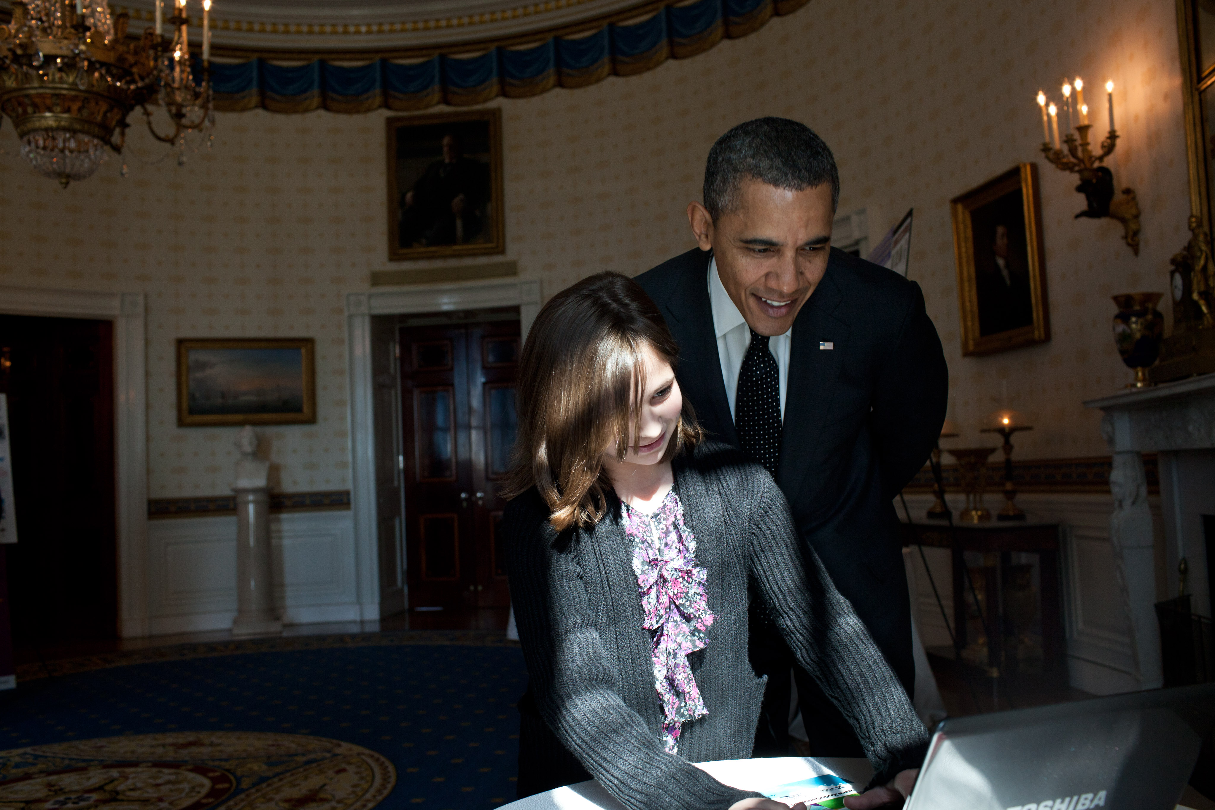 President Barack Obama looks over the shoulder of Hannah Wyman, 11, as she demonstrates her project in the Blue Room, Feb. 7, 2012, during the second annual White House Science Fair