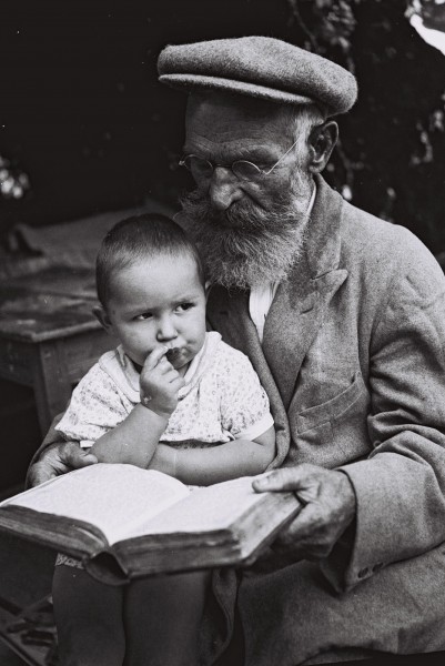 A DUTCH CONVERT TO JUDAISM WITH HIS GRANDCHILD IN HIS LAP, STUDYING THE BIBLE ON HIS FARM IN 