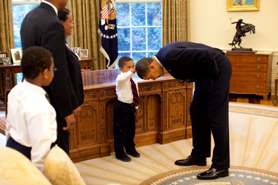 United States President Barack Obama bends down to allow the son of a White House staff member to touch his head