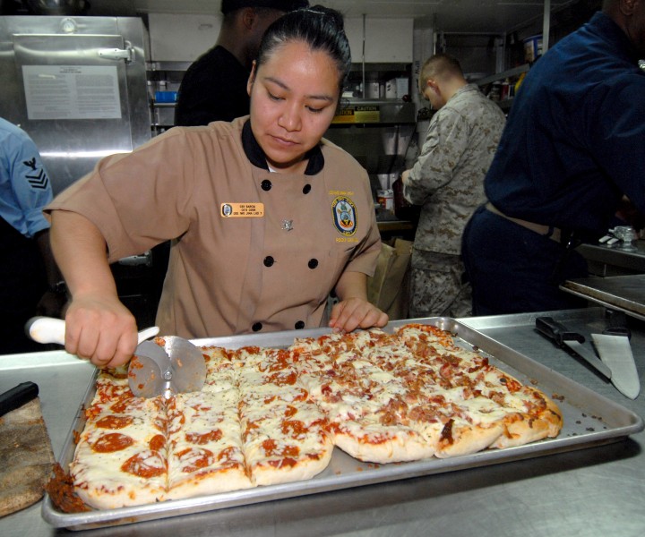 US Navy 060817-N-4856C-003 Culinary Specialist 3rd Class Elizabeth Garcia-Vargas slices pizzas for a pizza party in the ship's Flag Mess aboard the multi-purpose amphibious assault ship USS Iwo Jima (LHD 7)