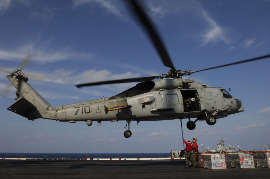 US Navy 061206-N-8591H-086 An air crewman watches as two aviation Ordnancemen connect a cargo pendant to a SH-60B helicopter