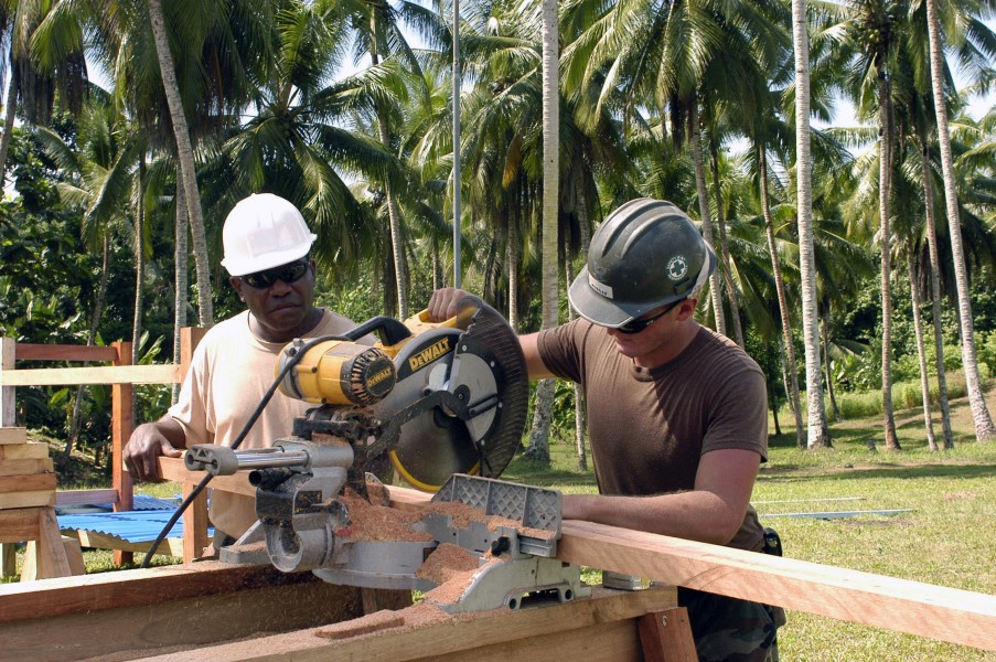 US Navy 070812-N-3901L-072 Builder 3rd Class Jeremy Morgan, assisted by a local villager, uses a table saw to cut lumber to repair the roof of the Panim Elementary School