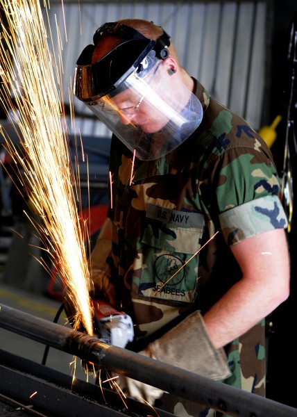 US Navy 100422-N-6357K-005 A Seabee grinds a pipe fitting to be used to fabricate a maintenance catwalk at a water treatment facility at Naval Station Rota, Spain