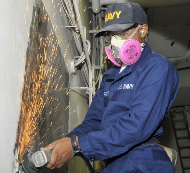 US Navy 101230-N-7103C-031 Aviation Electrician's Mate Airman Apprentice Emilio Burnett, from Coffeyville, Kan., uses a pneumatic grinder to remove