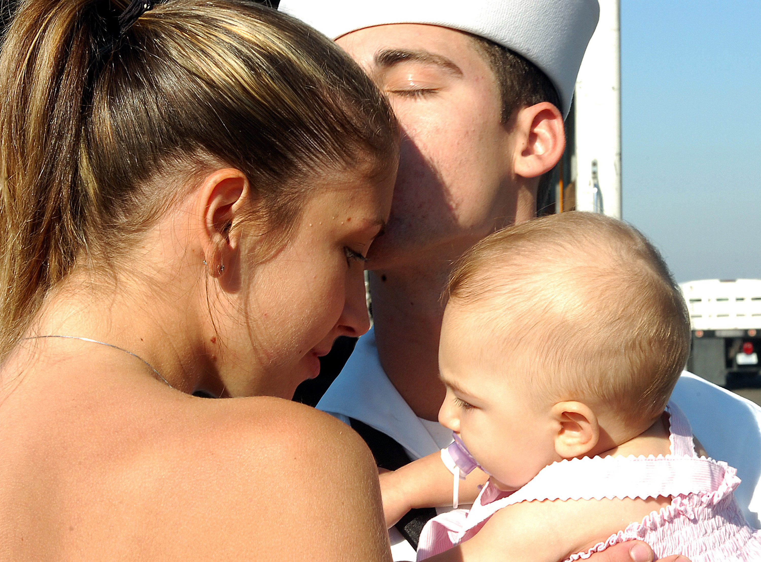 U.S. Navy Sailor embraces his wife and his 6-month-old daughter during a homecoming ceremony for USS Pearl Harbor (LSD 52) at Naval Base San Diego, California