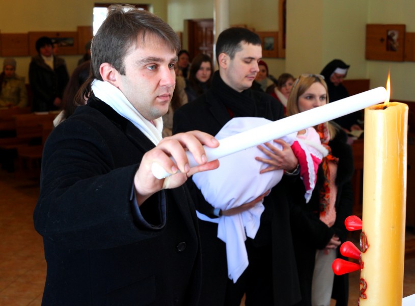 a godfather lighting up a candle during the christening of a baby-girl in the Catholic Church