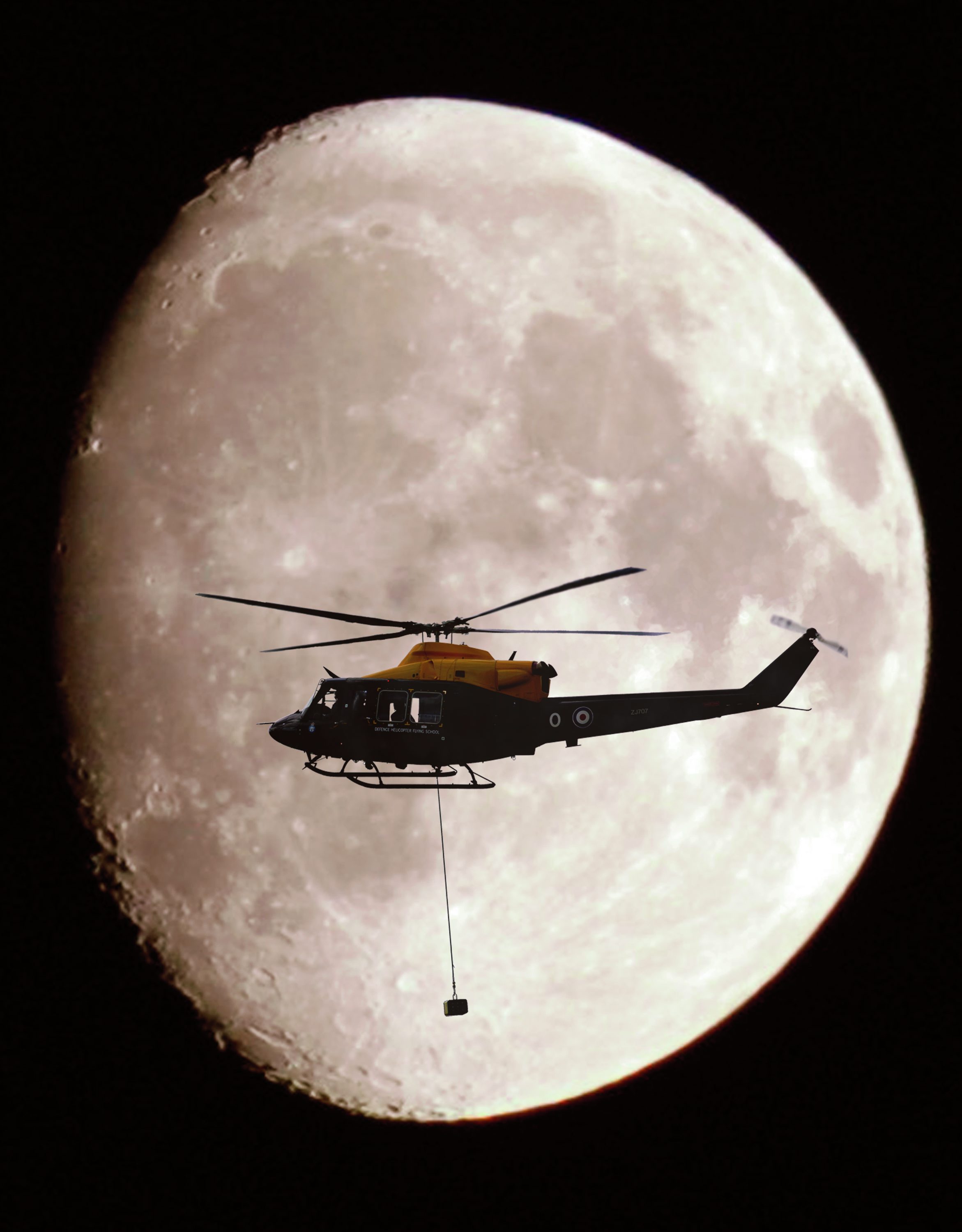 A Griffin Helicopter, with an underslung load, shown in silhouette against a full moon