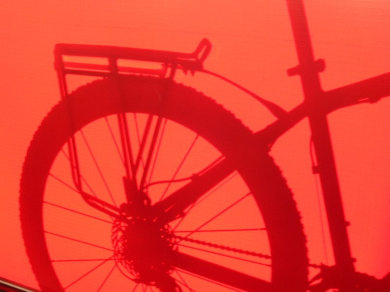 Silhouette of a bike leaning against a red canvas.