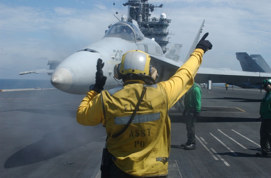 US Navy 030729-N-7732W-262 An Aviation Boatswain's Mate directs an F-A-18 Hornet onto a steam catapult during flight operations aboard USS John C. Stennis (CVN 74)