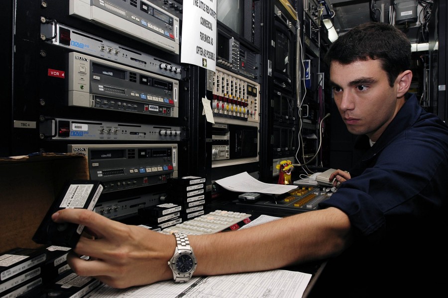 US Navy 050211-N-4166B-028 Journalist 3rd Class Michael Hart of Kingston, Tenn., grabs a video tape which will be played on the closed circuit television system ran by the Journalists twenty-four hours a day