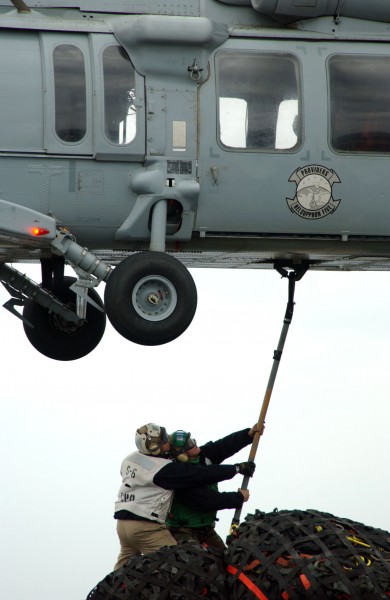US Navy 050312-N-5821P-120 Chief Storekeeper Israel Villones, left, braces Storekeeper Seaman Wesley Jacobs as he hooks on a cargo pendant onto the cargo hook of an MH-60S Seahawk aboard USS Kitty Hawk (CV 63)