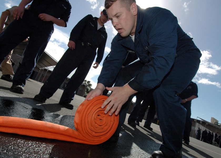 US Navy 051006-N-3019M-002 Damage Controlman Fireman Jason Robinson, assigned to the guided missile destroyer USS Paul Hamilton (DDG 60), rolls up a fire hose during the Damage Control Olympics